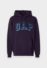 Felpa blu navy con tasca frontale a marsupio, cappuccio regolabile con cordino e bold "GAP" in tonalità di blu a contrasto. Materiale in cotone morbido.