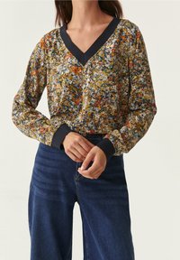 Floral long-sleeve blouse in multicolors, featuring a V-neck and navy cuffs. Paired with high-waisted blue denim jeans.