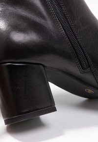 Schwarze Lederstiefelette mit glatter Oberfläche, seitlichem Reißverschluss und einem stabilen, quadratischen Absatz. Matte Sohle mit minimalem Branding.