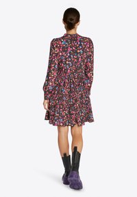 Černé květinové šaty s barevnými vzory, plisovaná sukně, dlouhé rukávy, vysoký límec, doplněné masivními černými a fialovými botami.