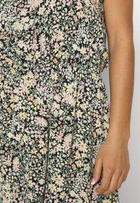 Sukienka w kwiatowy wzór w kolorze czarnym, ozdobiona różowymi i żółtymi kwiatami oraz zielonymi liśćmi. Elastyczny pas, miękka tkanina i fałdowany krój.