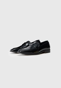 Schwarze Lacklederloafer mit elegantem, spitzem Design und doppelten Riemenakzenten. Profilierte Gummisohle für Stabilität und Komfort.