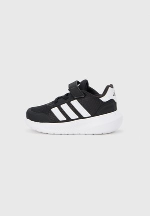 Black athletic shoe with breathable mesh upper, white three-stripe design, hook-and-loop strap, cushioned white sole, and textured accents.