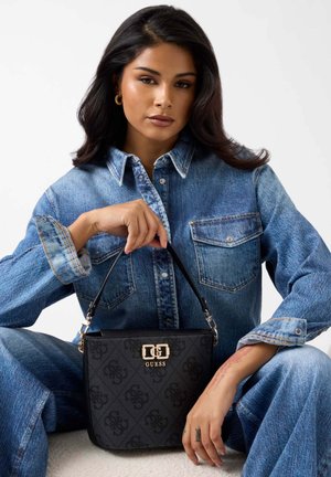 Zwarte Guess-handtas met een gestructureerd oppervlak, gouden hardware en een korte riem, gecombineerd met een blauw denim overhemd en bijpassende spijkerbroek.