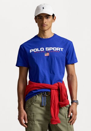 Sinine puuvillane T-särk, millel on "POLO SPORT" ja Ameerika lipp, koos oliivroheline taskupüksid. Punane kootud kampsun, mis on seotult vöö ümber. Valge kork.