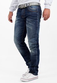 Jean bleu foncé avec légères décolorations, coutures contrastées, design ajusté, style à cinq poches, et une ceinture grise avec une boucle texturée.
