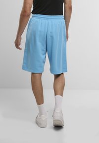 Light blue cotton shorts with an elastic waistband, reaching mid-thigh, paired with white sneakers and socks, viewed from behind.