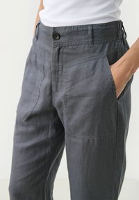 Pantaloni di lino grigi con una vestibilità rilassata, dotati di chiusura frontale con bottone, tasche laterali e una trama sottile.
