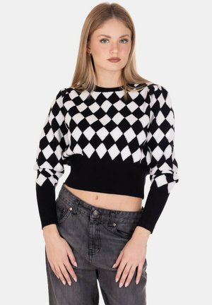 Maglione cropped in bianco e nero con un motivo a diamante, maniche a coste e una texture morbida; abbinato a jeans grigi a vita alta.