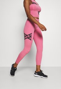 Top corto deportivo rosa y leggings con la marca negra de Nike. Los materiales parecen elásticos y ajustados. Llevado con zapatillas negras.