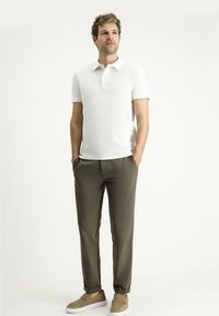 Polo bianco a maniche corte, pantaloni verde oliva e scarpe slip-on marrone chiaro. Tessuto morbido, design rilassato. Posizione in piedi.