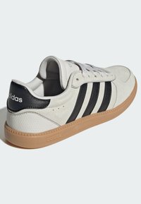 Bijele kožne tenisice s crnim antilop prugama, vezicama i gumiranim potplatom boje gume. Logo na peti i boku, korišteni materijali s teksturom.