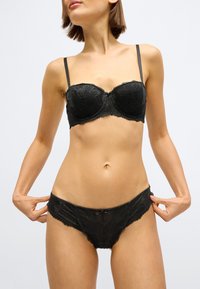 Črni komplet spodnjega perila iz čipke s balconette nedrčkom z obrobo in nastavljivimi naramnicami ter ujemajočimi čipkastimi hlačkami, oboje z rožnatim vzorcem.