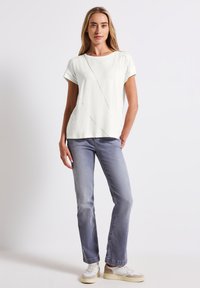 Hvid kortærmet top med skrå syninger, parret med lysegrå lige jeans og sneakers med lagdelte farver.