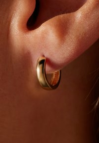 Gouden oorbel in de vorm van een hoepel, bevestigd aan een oorlel, met een gladde, glanzende oppervlakte en een cirkelvormige gesloten ontwerp.