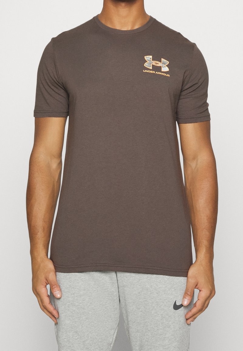 Brun kortärmad t-shirt i bomullsmix med en orange och grå Under Armour-logotyp på vänster bröst.