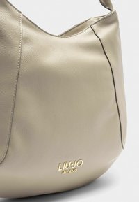 Borsa a tracolla in pelle beige con una texture liscia, cuciture sottili e un logo impresso in oro "LIU JO MILANO" nella parte inferiore.