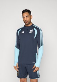 Ναυτικό μπλε αθλητική φανέλα με ανοιχτό μπλε λεπτομέρειες, μακριά μανίκια, ψηλό γιακά και λογότυπο της ομάδας στο στήθος; συνδυάζεται με αντίστοιχο σορτς.