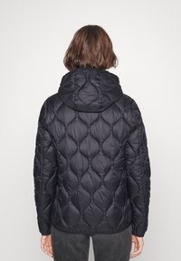 Giubbotto imbottito nero con cappuccio e motivo trapuntato, caratterizzato da una texture liscia e una vestibilità rilassata. Il design include polsini elasticizzati sulle maniche.