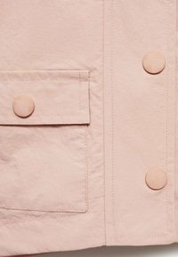 Giacca rosa chiaro in tessuto testurizzato, con due bottoni rotondi e una tasca frontale con pattina. Dettagli di cucitura pulita.