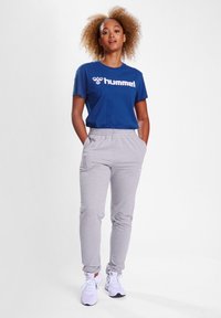 Blå bomulds t-shirt med hvidt logo, parret med grå sweatpants med sidelommer og elastisk talje. Hvide sportssko.