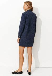 Robe bleu marine avec imprimé léopard, manches longues et col. Présente des poignets à boutons et de légers fentes sur les côtés. Associe avec des ballerines noires cloutées.
