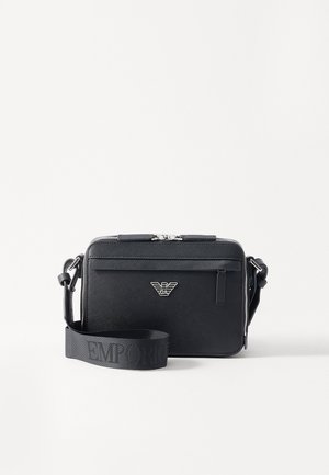 Melnā plecu soma, izgatavota no teksturēta materiāla. Iekļauj rāvējslēdzēja aizdari, priekšējo rāvējslēdzēja kabatu un metāla logotipa akcentu. Ietver regulējamu siksnu.