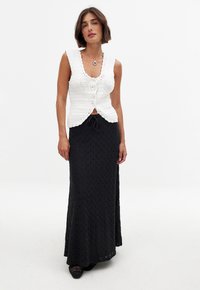 Un crop top blanc en tricot avec des bords festonnés et un détail de boutons, associé à une longue jupe maxi noire texturée avec une taille à cordon.