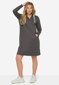 Robe hoodie grise avec une poche avant et des fentes sur les côtés. Dotée de cordons de serrage à motif vert. Tissu texturé, longueur au-dessus du genou.