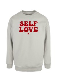 Felpa grigia chiara in cotone, con la scritta rossa in grassetto "SELF LOVE" con lettere arrotondate e un piccolo cuore come accento sottostante.