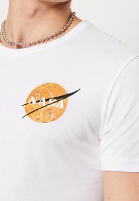 Camiseta blanca de algodón con un logo de NASA en naranja y un swoosh negro. Mangas cortas y diseño clásico de cuello redondo.