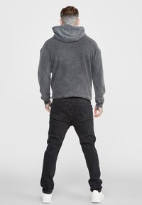 Felpa grigia con una texture comoda e jeans neri abbinati. L'outfit presenta una vestibilità rilassata e un cappuccio con cordino, abbinato a sneakers bianche.