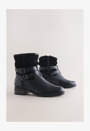 Juodi odiniai kulkšnies ilgio batai su zomšos apvadais, dviem dirželiais su sagtimis ir siuvinėta tekstūra šone; turi šoninį užtrauktuką patogiam užsidėjimui.