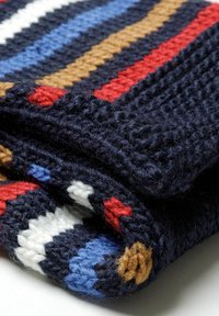 Couverture tricotée avec des rayures navy, rouge, blanc, bleu et marron. Présente un tissage texturé et épais avec des bords à franges.