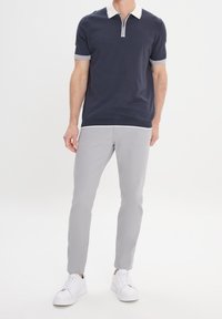 Granatowa koszulka polo z krótkim rękawem, z zamkiem błyskawicznym i szarymi wykończeniami, połączona z jasnoszarymi spodniami w slim fit oraz białymi trampkami.