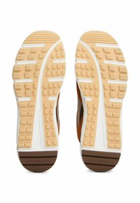 Semelles de chaussures de sport en suede marron avec une texture en caoutchouc pour l'adhérence, affichant un intercalaire blanc et un motif de traction alterné en tan et blanc.