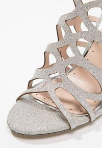 Silver glitter open-toe sandal with cutout design, smooth inner lining, and flat sole. Notable shine and textured surface.