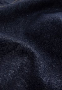 Primo piano di tessuto denim blu scuro che mostra la trama e il motivo tessuto con un leggero scolorimento e una cucitura visibile.