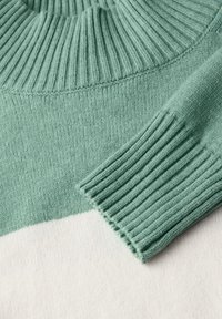 Maglione a maglia con collo e polsini verdi a coste, con un corpo bianco. Morbido al tatto, design semplice e contrasto di colori.