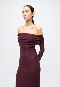 Burgundy lace dress with an off-the-shoulder neckline, textured floral pattern, fitted silhouette, and long sheer sleeves.