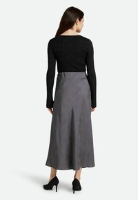 Schwarzes Langarmoberteil in Kombination mit einem grauen gemusterten Midikleid. Der Rock besitzt eine glatte Textur und ein dezentes Blätterdesign und wird mit schwarzen High Heels getragen.