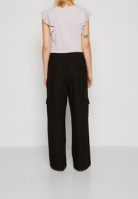 Světle fialový top s řasenými rukávy, spárovaný s černými širokými kargo kalhotami s bočními kapsami a měkkou, texturovanou tkaninou.