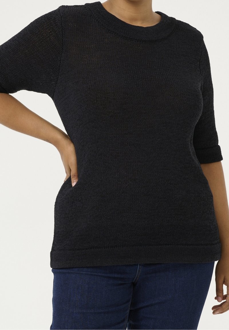 Knitted black pullover with short sleeves, round neckline, and textured pattern. Features side pockets and a relaxed fit, paired with dark jeans.