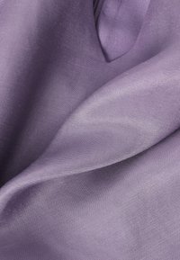 Tissu lavande lisse avec une fine texture de tissage diagonal, légèrement plié pour montrer les reflets de la lumière et les ombres subtiles.