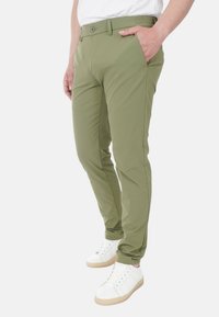 Pantaloni verde oliva con vestibilità slim, realizzati in materiale leggero, con chiusura a bottone e tasche laterali, abbinati a sneakers bianche.