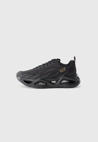 Black EA7 sneaker with breathable mesh upper, wave-like design, thick sculpted sole, and gold logo on side, shown from a side view.