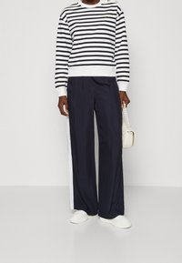 Felpa a righe blu navy e bianca con scollatura a girocollo e dettagli con bottoni, abbinata a pantaloni larghi blu navy con una striscia laterale bianca.