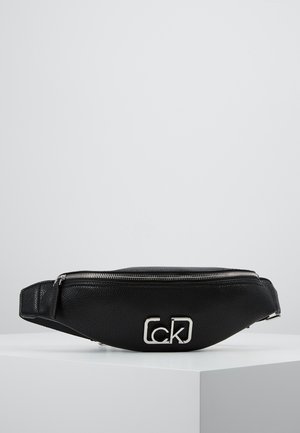 Czarna skórzana nerka o fakturowanej powierzchni z srebrnym zamkiem błyskawicznym i srebrnym logo „ck” na przodzie, prezentowana na białym pedestale na szarym tle.