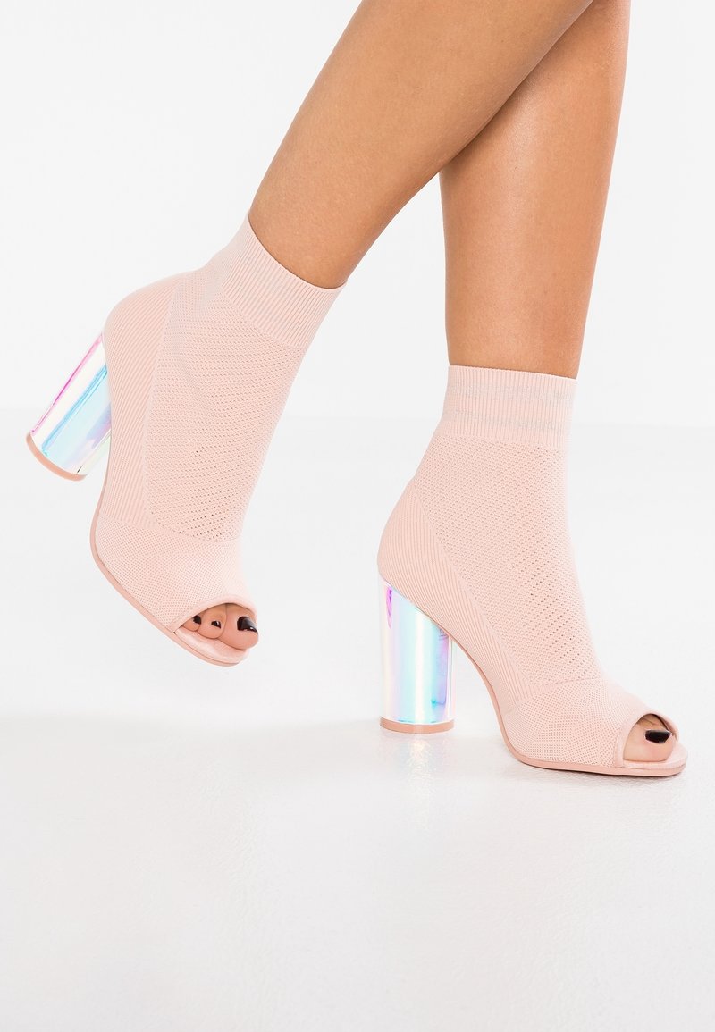 Botines de punto rosa con puntas descubiertas y un tacón grueso reflectante e iridiscente. Textura suave con un diseño ajustado, que eleva el estilo.