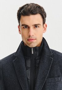 Ciemnoszara wełniana kurtka o kołnierzowym kroju na czarną pikowaną kurtkę. Posiada zamek błyskawiczny oraz fakturowane tkaniny w całej konstrukcji.